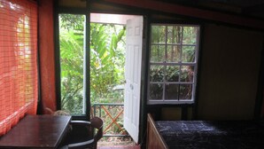 Una habitación con cama, escritorio y silla. Se ve follaje verde por la ventana.