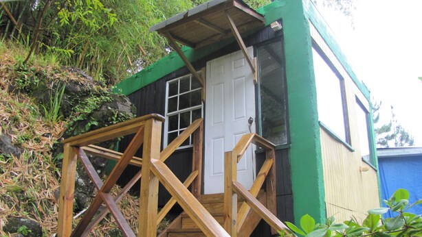 Una escalera de madera conduce a un pequeño edificio de madera con una puerta blanca y ventanas.