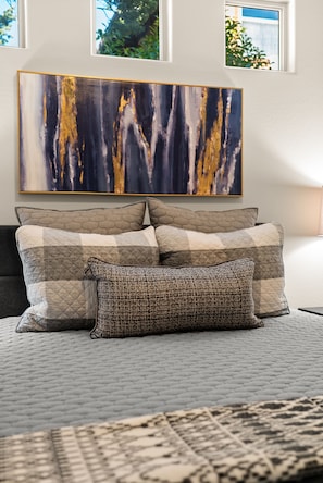 Relax in a serene bedroom with a large abstract painting above the bed, featuring a mix of pillows in various shades.