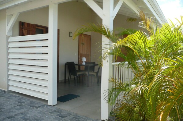 A covered outdoor area with a dining table and chairs, a wooden door, and a palm plant.