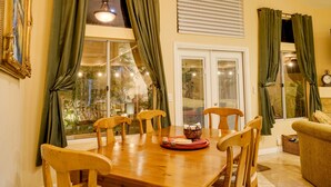 A dining area with a wooden table and chairs, a basket with bread, and a view of greenery through the window.