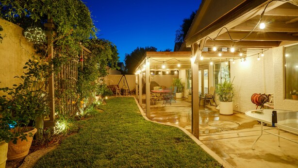 A covered patio area with a lawn, outdoor furniture, and string lights.