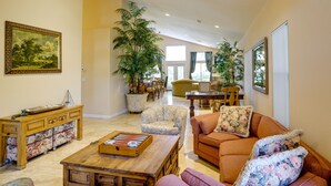 A spacious living room with a wooden coffee table, floral armchairs, and a sofa with decorative pillows. A dining area with a table and chairs is visible in the background.