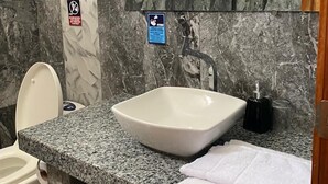 Un baño con lavamanos blanco, paredes de mármol, toallero y retrete.