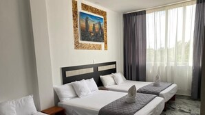 Habitación de hotel con tres camas, un cuadro en la pared y un ventanal con cortinas.