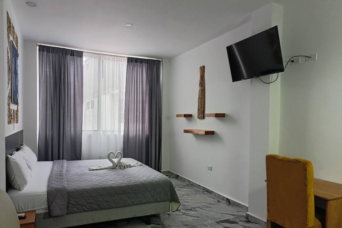 Ein modernes Hotelzimmer mit Bett, einem an der Wand befestigten Fernseher und einem Schreibtisch mit Stuhl.