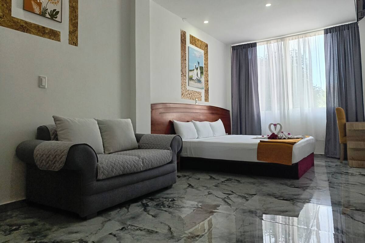 Ein Hotelzimmer mit Bett, einer Couch, einem hölzernen Kopfteil, einem Marmorboden und einem Fenster mit Vorhängen.