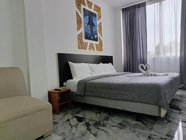 A hotel room with a bed, a nightstand, a chair, and a wall-mounted picture.