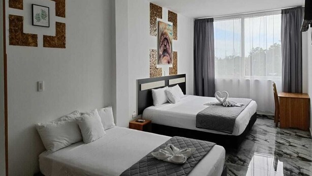 Habitación de hotel con dos camas, un ventanal con cortinas, un televisor de pantalla plana y obras de arte en las paredes.