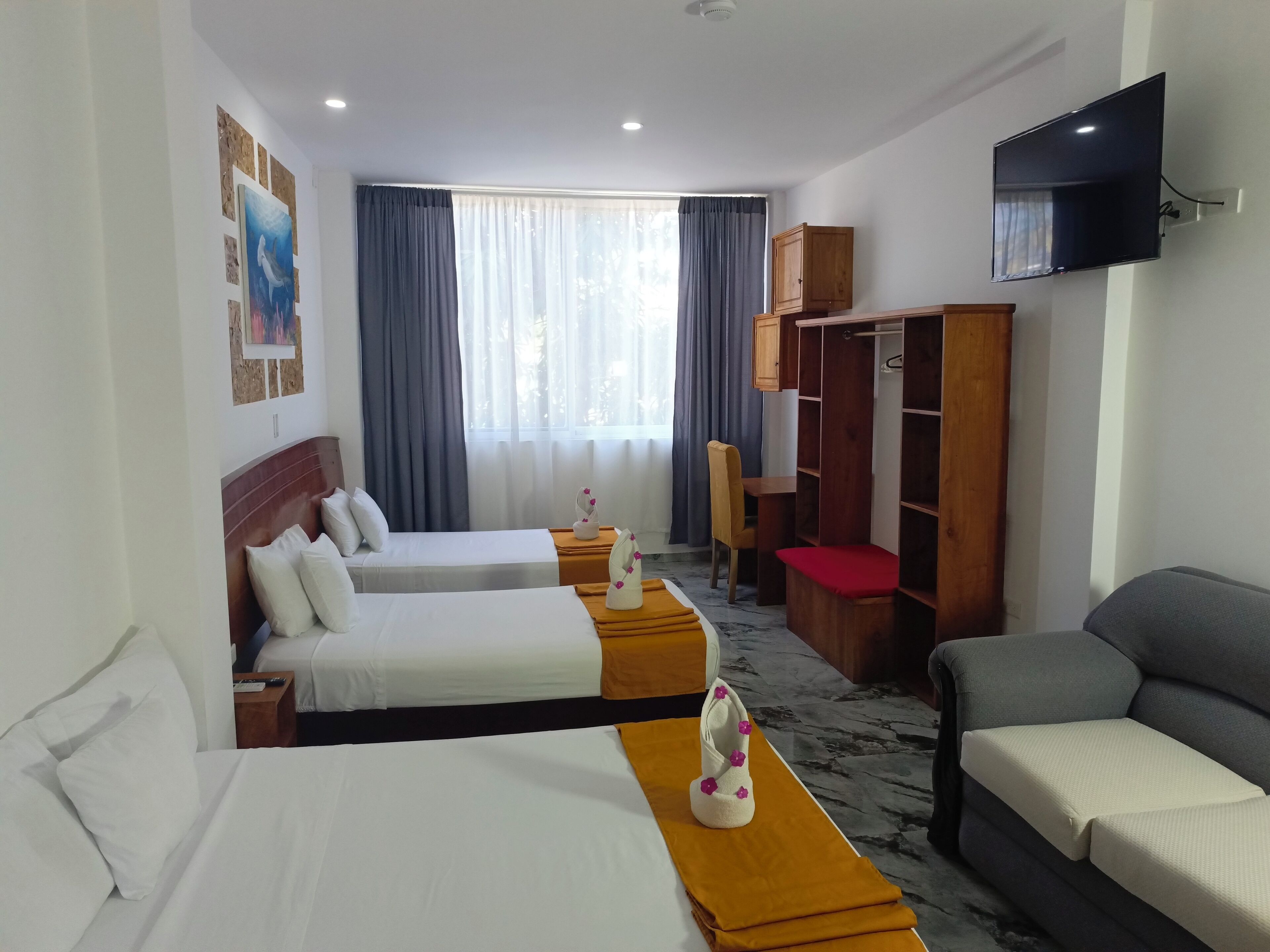 A hotel room with two beds, a sofa, a TV, a wardrobe, and a desk.