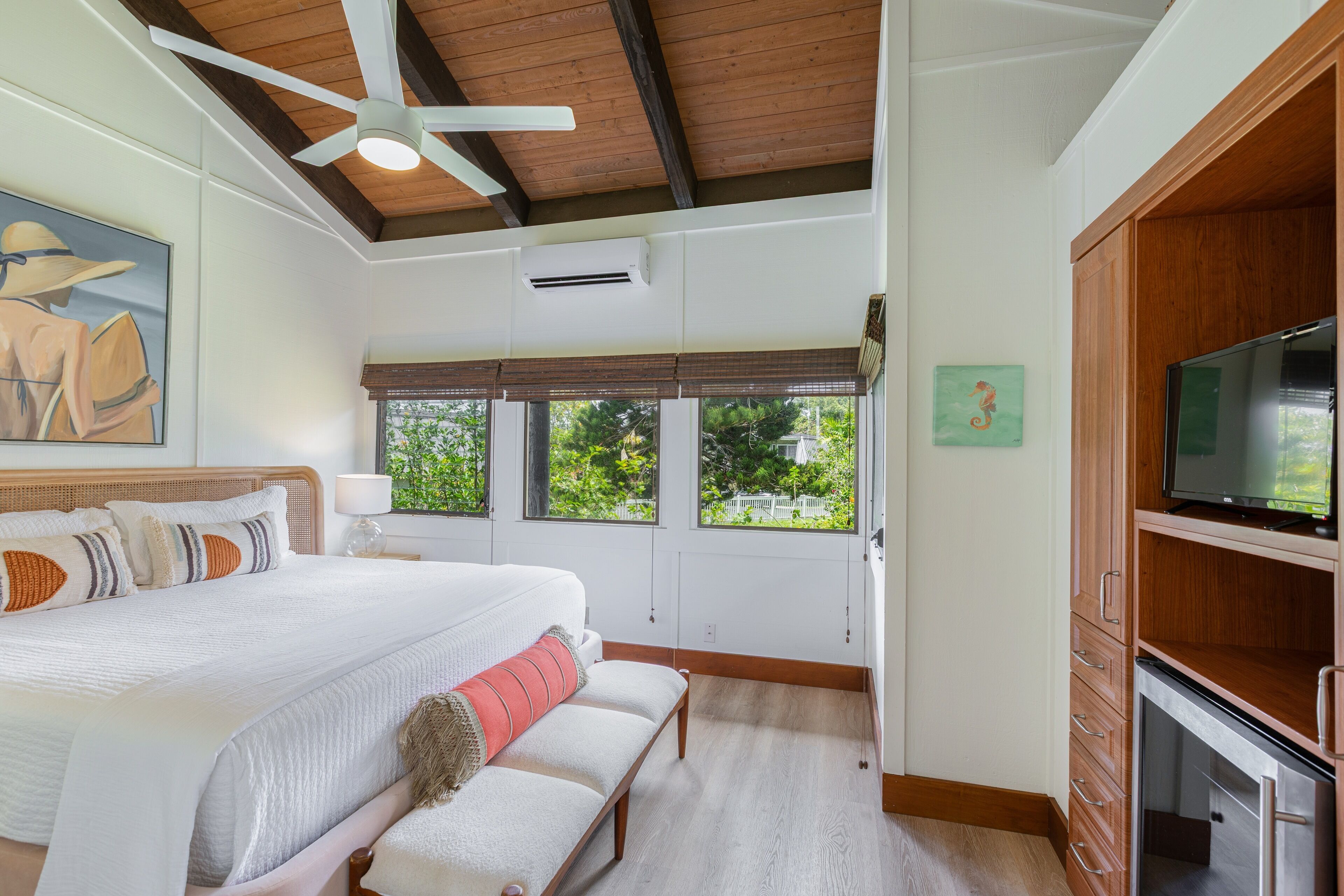 A bedroom with a large bed, a bench, a ceiling fan, and a TV.