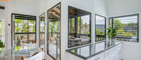 A modern kitchen with large windows, a glass dining table, and white cabinetry.