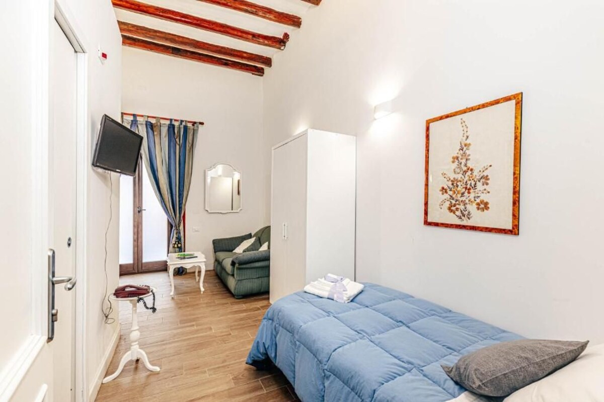 Quarto com cama, poltrona, televisão e guarda-roupa.