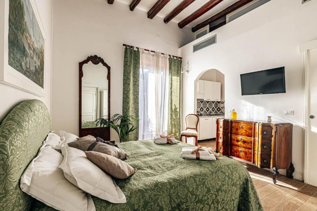 A bedroom with a bed, a dresser, a television, and a window with curtains.