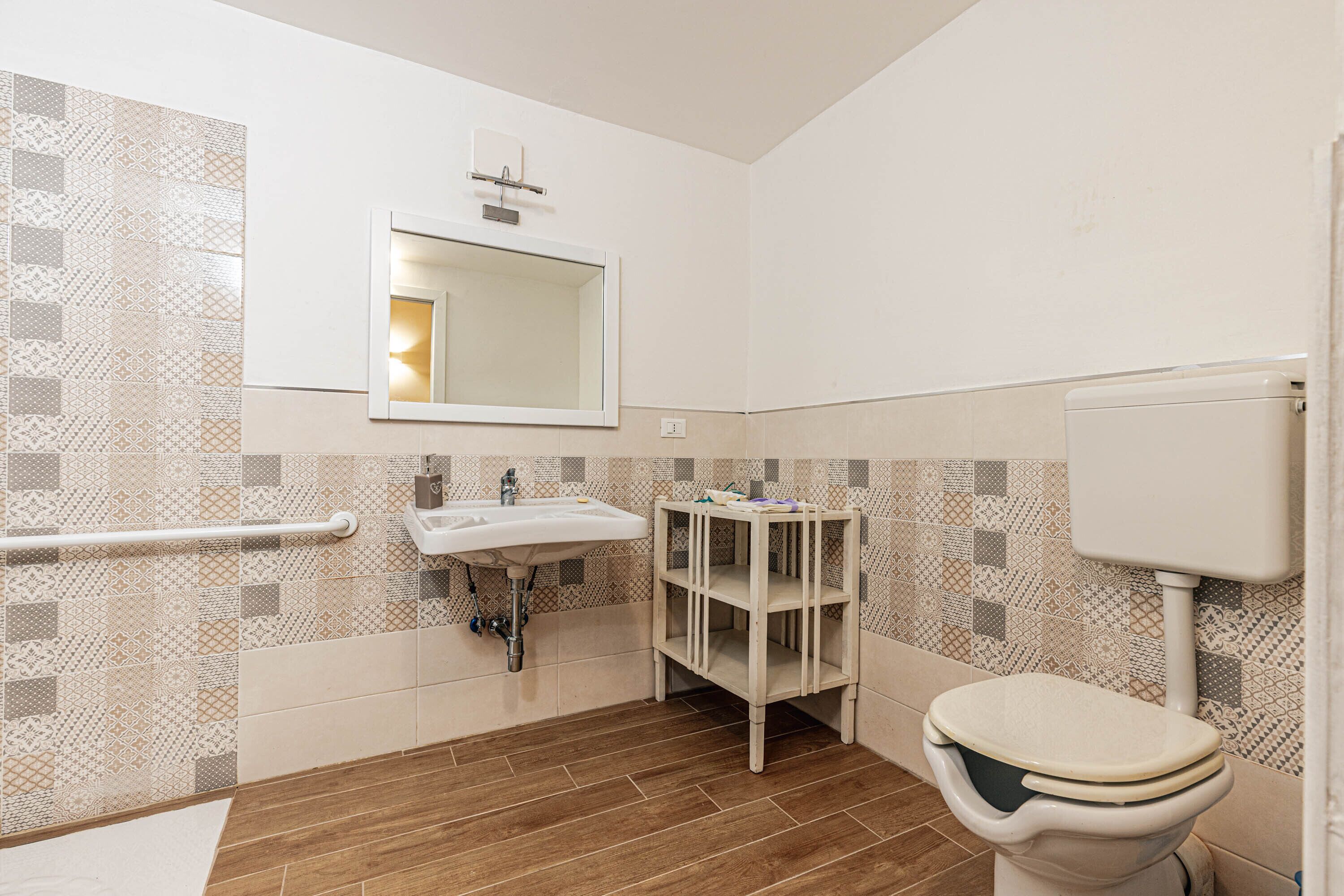 A bathroom with a sink, mirror, toilet, and patterned tiles.