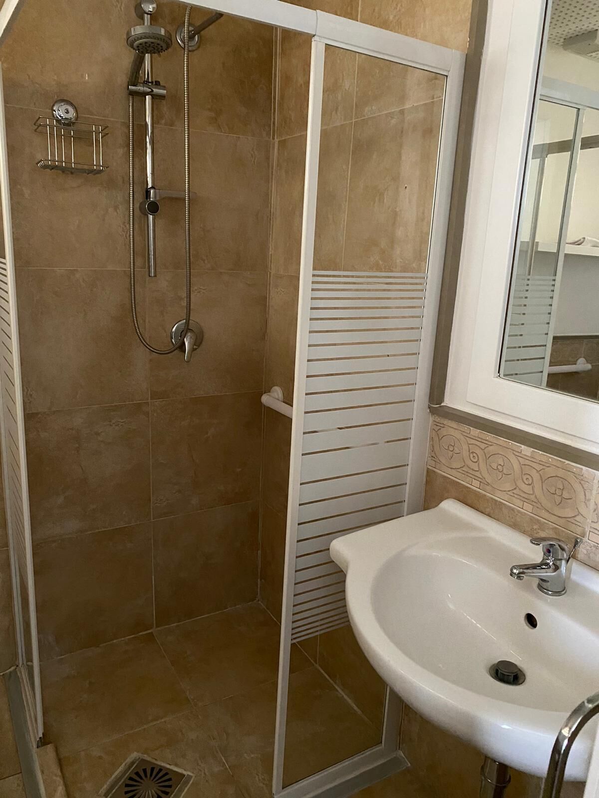 Een badkamer met douche, wastafel en spiegel.