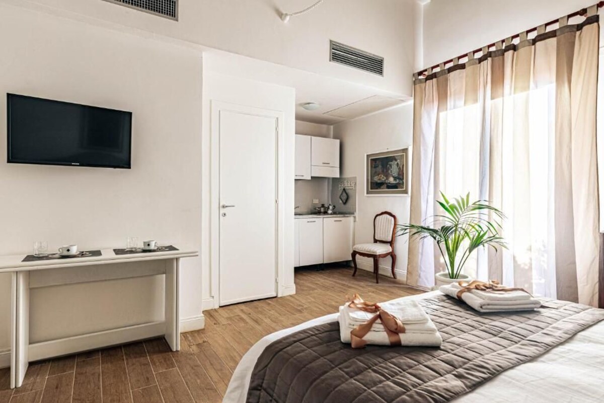 Une chambre d’hôtel avec un lit, un bureau, une télévision, une chaise et une plante en pot.