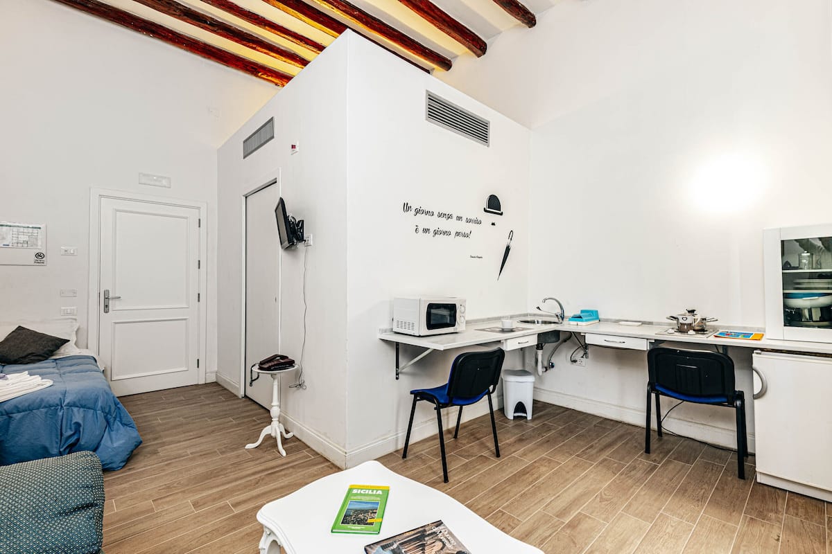 A compact hotel room with a bed, a desk, a chair, a microwave, and a sink.