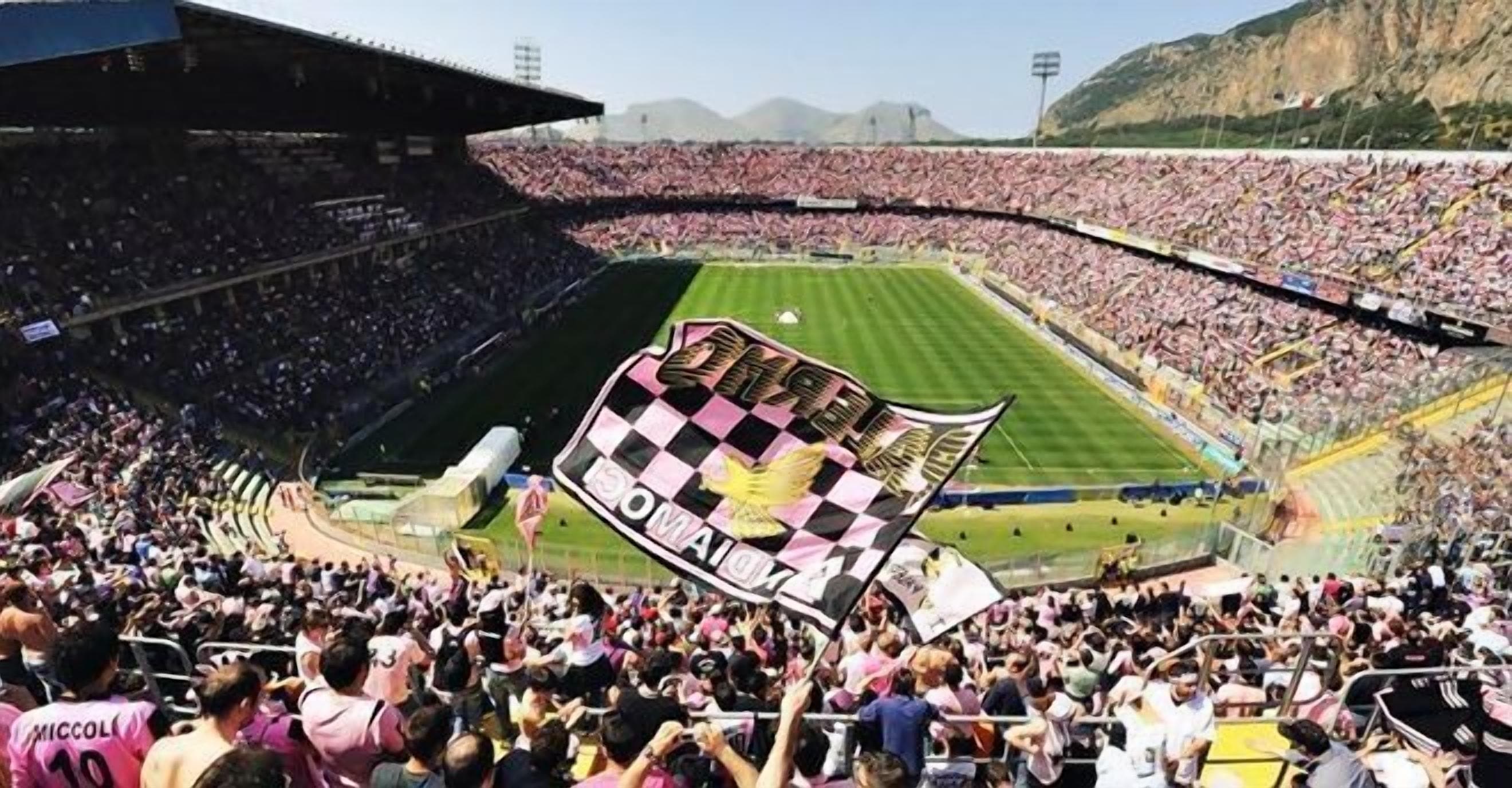 Un estadio lleno de espectadores, una gran bandera a cuadros y montañas al fondo.