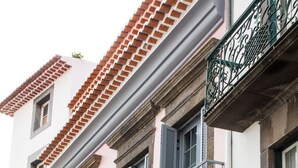 A multi-story building with a pink facade, multiple balconies with metal railings, and shutters on the windows. - Apartamentos Funchal by Petit Hotels (Funchal)