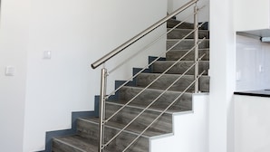 A modern staircase with metal railings and wooden steps, leading to a kitchen area with white cabinetry. - Apartamentos Funchal by Petit Hotels (Funchal)