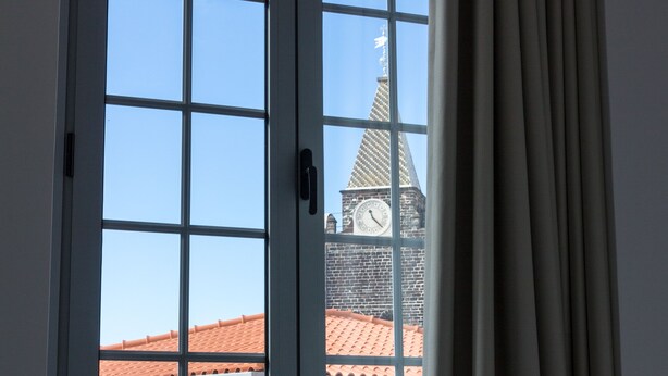 A window with a view of a building with a clock tower and a red-tiled roof. - Apartamentos Funchal by Petit Hotels (Funchal)
