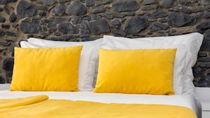 A bed with white and yellow bedding against a stone wall. - Apartamentos Funchal by Petit Hotels (Funchal)