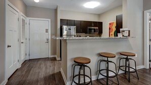 A kitchen with a refrigerator, microwave, and cabinets, a door, and three stools. - 2Bd 2bth *1 mile walk to downtown!* #401 (Nashville)