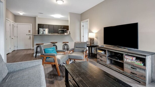 A living room with a sofa, two armchairs, a coffee table, a TV, and a kitchen area with cabinets and appliances. - 2Bd 2bth *1 mile walk to downtown!* #401 (Nashville)