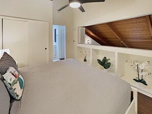 Ein Schlafzimmer mit einem Bett, einem Deckenventilator, einer weißen Tür und einem kleinen weißen Regal mit Pflanzen.