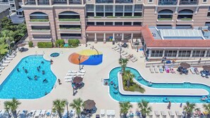 Un hotel con varias piscinas, tumbonas y una fuente central.