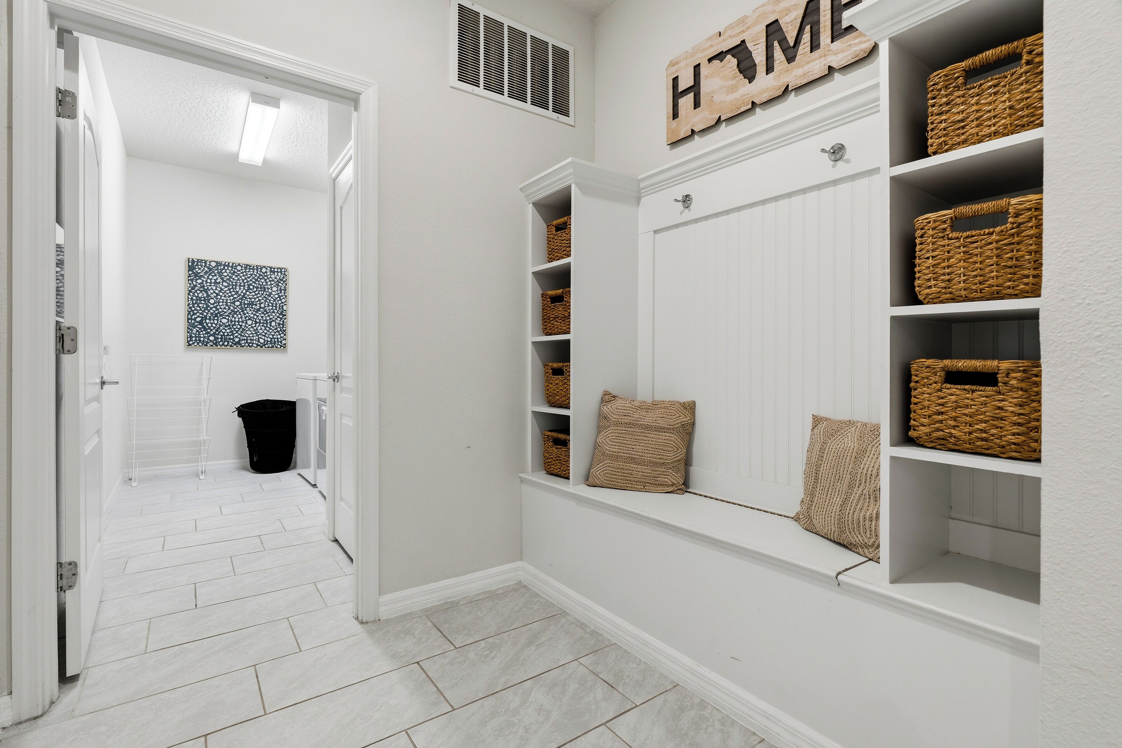 A hallway with a white door, a black trash bin, wicker baskets on shelves, and a 'HOME' sign on the wall.