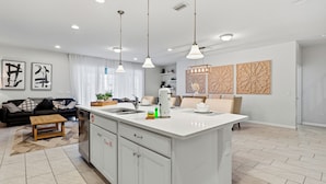 Uma cozinha moderna com ilha central, armários brancos e iluminação pendente.