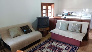 A living room with a sofa, a television, and a kitchen area in the background.