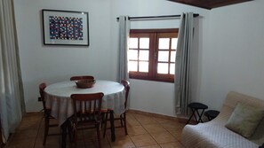 A dining area with a round table, chairs, a basket, and a window with curtains.
