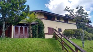Una casa de dos pisos con una escalera de madera que lleva a la entrada, rodeada de follaje y árboles.