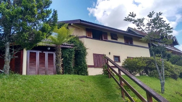 A two-story house with a wooden staircase leading to the entrance, surrounded by greenery and trees.