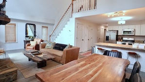 Amplia sala de estar con una mesa de comedor de madera, un sofá y una escalera que lleva a un nivel superior.