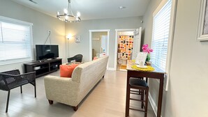 A living room with a sofa, a TV, a dining table with chairs, and a chandelier.