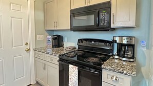 A kitchen with white cabinets, a black stove, a microwave, and a coffee maker.