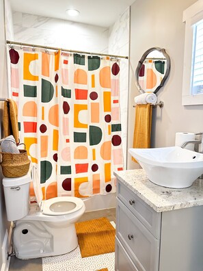 A bathroom with a toilet, a sink, a mirror, and a shower curtain with a geometric pattern.