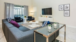 Ein modernes Wohnzimmer mit einer grauen Eckcouch, einem Glastisch und einem flach an der Wand befestigten Flachbildfernseher.