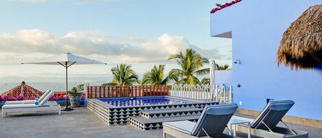 A rooftop pool area with lounge chairs, a pool, and a view of palm trees and mountains.