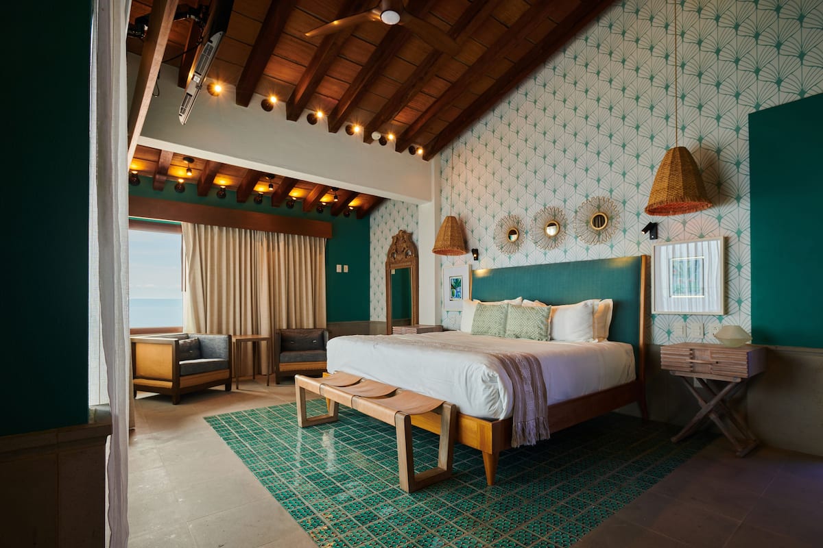 Un dormitorio amplio con una cama grande, un banco, un sofá y vistas al mar.