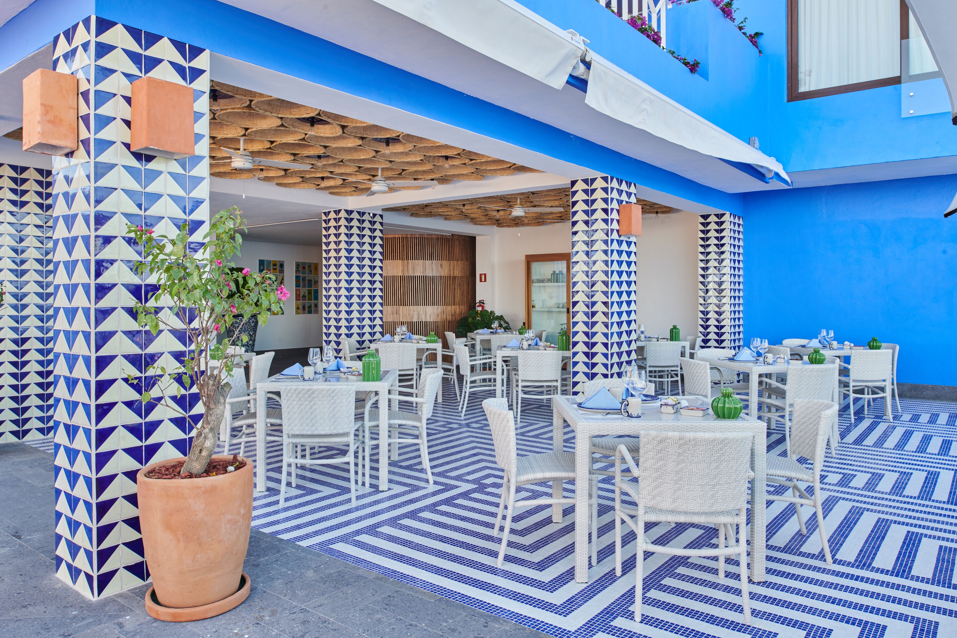 An outdoor dining area with white wicker furniture and blue patterned flooring.