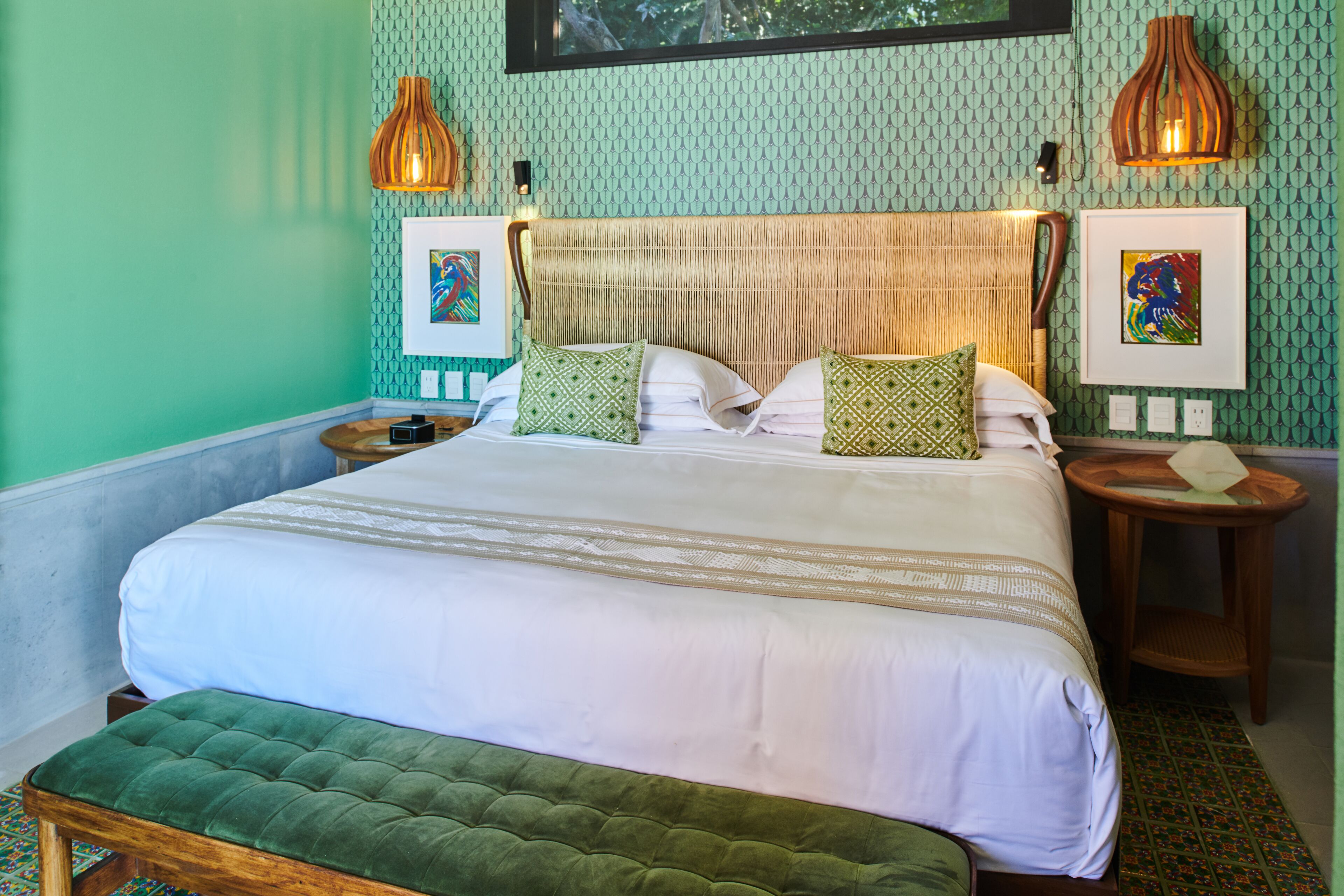 A neatly made bed with a green upholstered bench, a woven headboard, and two bedside lamps.
