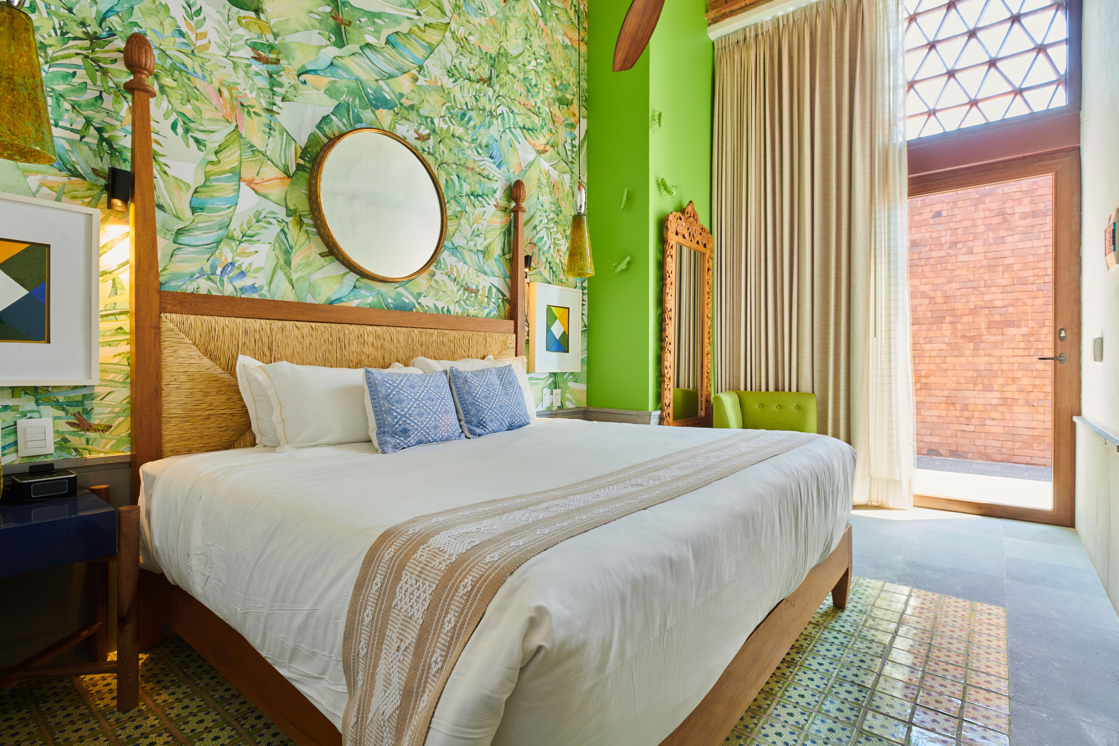 A large bed with a wooden headboard, a green accent wall, and a large window with curtains.