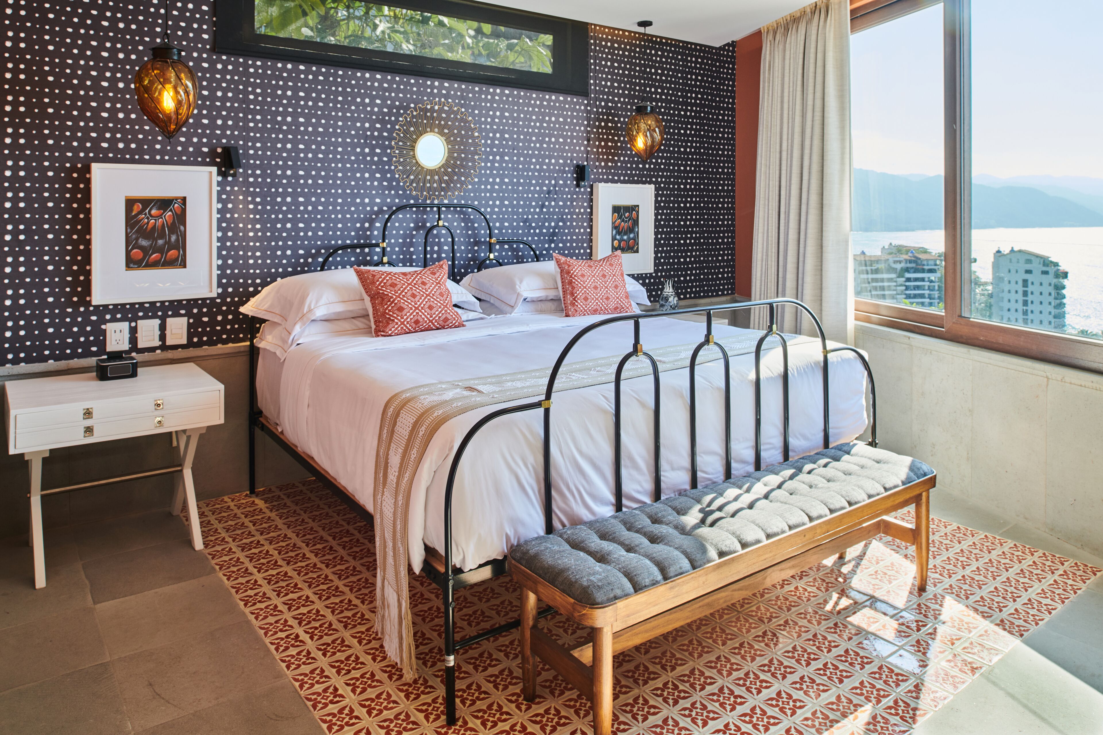 Een moderne slaapkamer met een groot bed, een nachtkastje, een bankje en uitzicht op de stad.