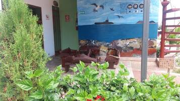 A building with a mural of birds and a ship, outdoor seating, and green plants.