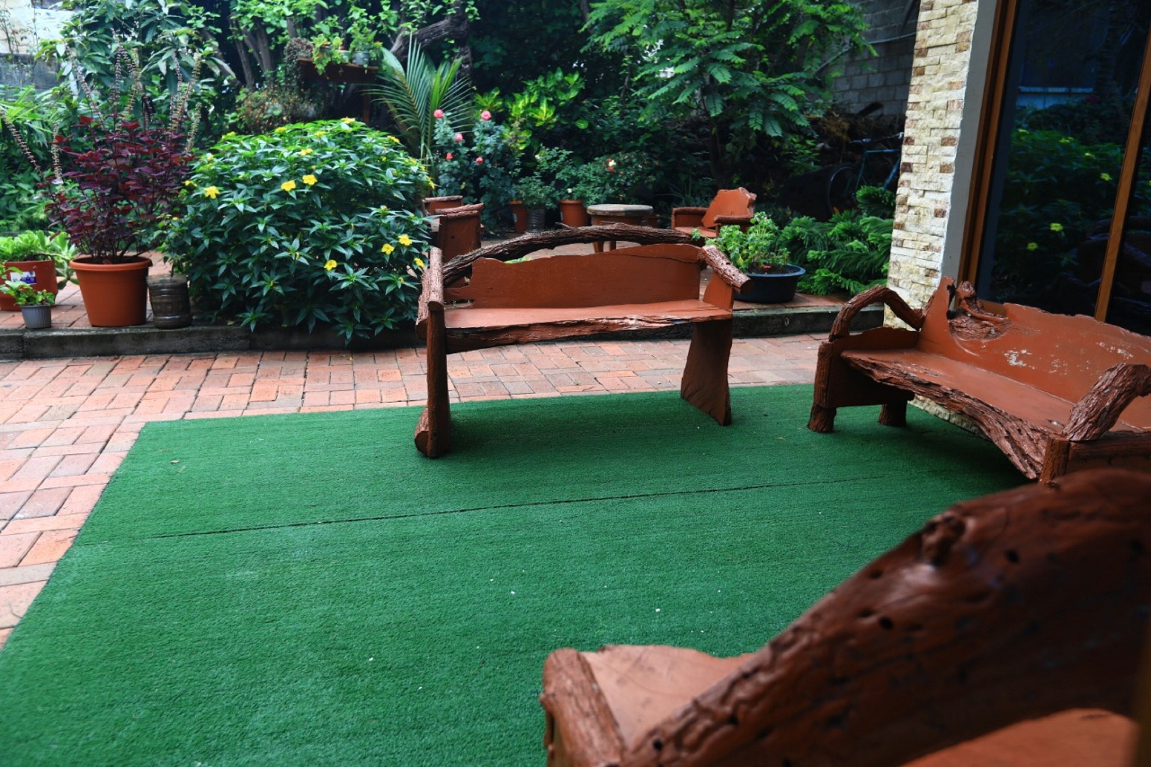 Un espace extérieur aménagé avec un banc en bois et une table, entouré de plantes en pot et d’un mur en briques.